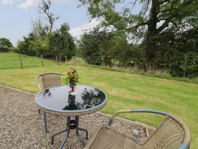a glass table with a bouquet of flowers on it next to two chairs at Sweet Briar Shepherds Hut in Brecon