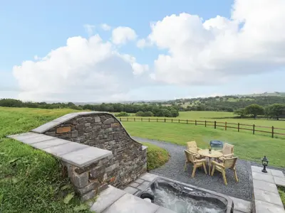 a stone fire pit with a table and chairs next to a field at Tan Y Wawr - Derwen in Welshpool