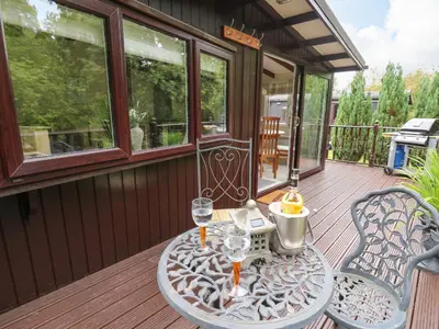 a wooden deck with a table with wine glasses on it at Riverside Rest in Builth Wells