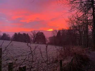a sunset in a snowy field with a red sky at Cwmbach Cottage, Hay on Wye in Glasbury