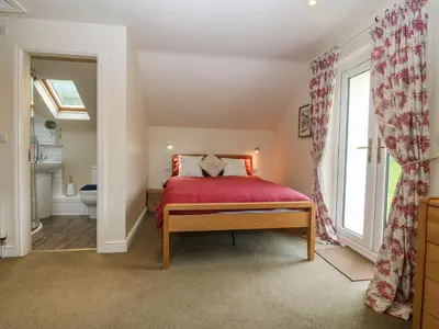 a bedroom with a red bed and a bathroom at Tyn Llwyn in Talsarnau