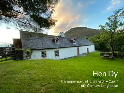 an old white house on a field with a bench at Longhouse - Hen Dy in Rhayader