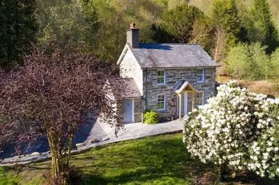 a small stone house with flowers in front of it at Charming Riverside Cottage in Snowdonia National Park in Tanygrisiau
