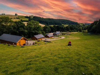 a person is sitting in a field near a house at Cherry Cabin - Little Log Cabin in Wales in Bettws Cedewain