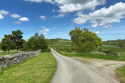 a road in a field with a stone wall at Camlad Barn in Chirbury