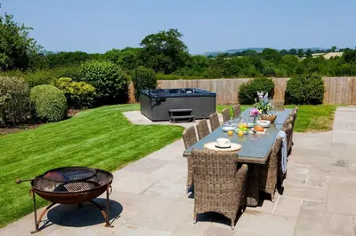 a patio with a table and chairs and a grill at Roundton Farmhouse in Chirbury
