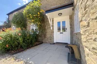 a stone house with a white door and a bench at Roundton Farmhouse in Chirbury