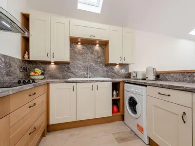a kitchen with white cabinets and a washer and dryer at Parlwr Godro - Uk41513 in Llanfair Clydogau
