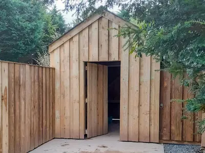 a wooden shed with a large door next to a fence at Brynog Mansion Apartment in Cilcennin