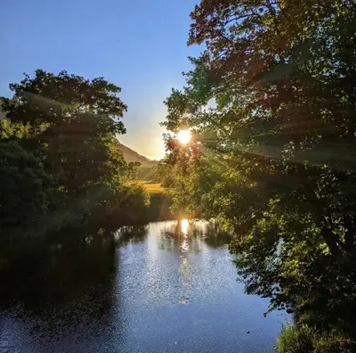 a view of a river with the sun shining through trees at Dove Cottage in Newbridge on Wye