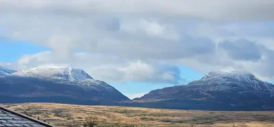 two snow capped mountains with a house in the foreground at Log cabin - free parking garden & pet friendly in Trawsfynydd