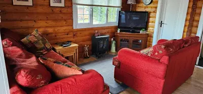 a living room with two red chairs and a television at Log cabin - free parking garden & pet friendly in Trawsfynydd