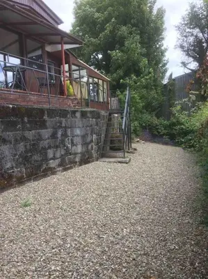 a building with a balcony and a stone wall at Riverside Chalet in heart of Lampeter, West Wales in Lampeter