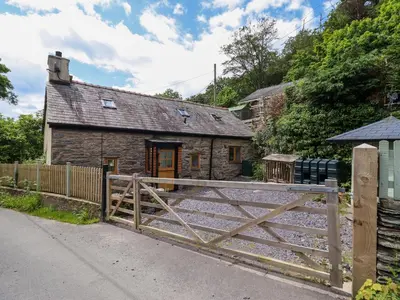 a stone cottage with a wooden gate in front of it at Hen Bopty in Fairbourne