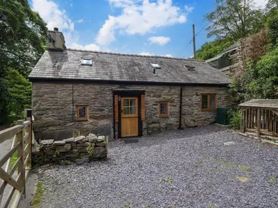 a stone cottage with a wooden door on a gravel driveway at Hen Bopty in Fairbourne