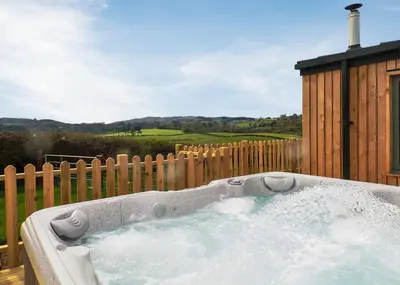 a hot tub in a backyard with a wooden fence at Castle Pren Lodges in Llanddewi Ystradenny