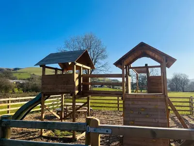 a wooden playground with a slide in a fence at Caban Nant Ddu in Nantmel
