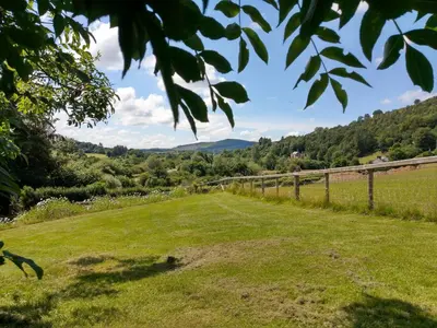 a field with a fence and mountains in the background at Seven Stars- hot tub & garden with fabulous views. in Llandrindod Wells
