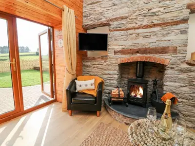 a living room with a stone fireplace with a tv at Tegfan Barn in Pant-y-dwr