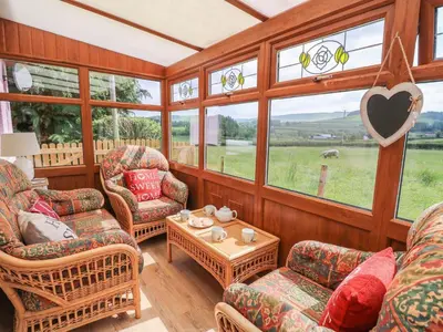 a living room with chairs and a table and windows at Tegfan Bungalow in Pant-y-dwr