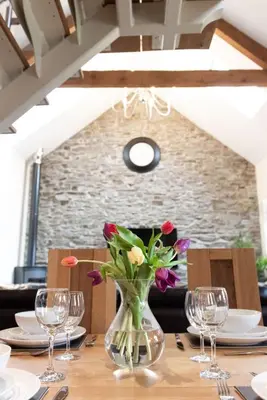 a vase of flowers on a table with glasses at Yr Hen Beudy in Aberystwyth