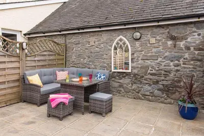 a patio with a table and chairs and a stone wall at Yr Hen Beudy in Aberystwyth