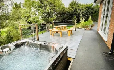 a hot tub on a deck with a picnic table at Ger Yr Afon in Saint Harmon