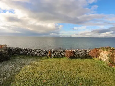 a dog standing next to a stone wall next to the ocean at Bramble Bank in Harlech