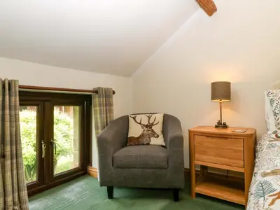 a bedroom with a chair with a deer pillow on it at Redstart Cottage in Leominster