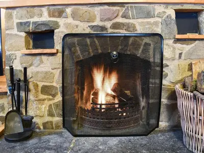 a stone fireplace with a fire in it at Gwynfan Bungalow in Llandrindod Wells