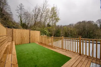 a wooden deck with a green lawn on it at BROOK HOUSE 4a in Llangollen