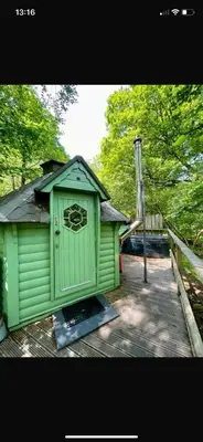 a green shed sitting on top of a wooden deck at Woodland Cabin with Private Hot Tub in Barmouth