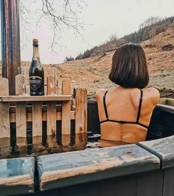 a woman sitting at a table with a bottle of beer at Oak SPECIAL WINTER OFFERS - Hot tub in Barmouth