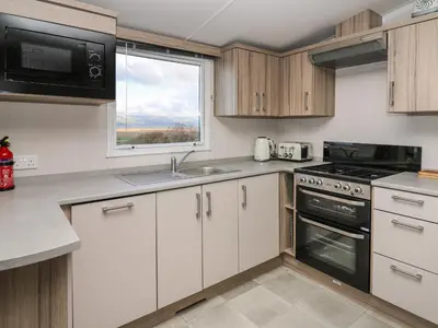 a kitchen with white cabinets and a window at Gwent 74 in Borth