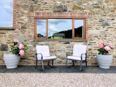 two chairs and flowers sitting in front of a stone wall at Cwmwr in Pen-y-bont-fawr