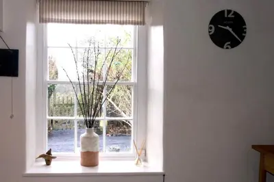 a window with a vase on a window sill with a clock at Glan y Morfa Welsh farmhouse overlooking Dyfi Estuary Rated 4 star Visit Wales in Pennal