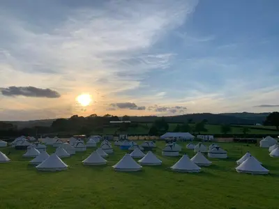 a group of white tents in a field with the sunset at Fred's Yurts at Hay Festival in Hay-on-Wye
