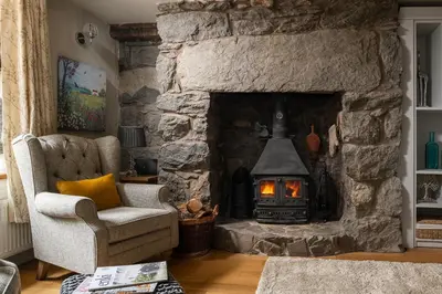 a stone fireplace in a living room with a chair at Ysgoldy in Llanfor