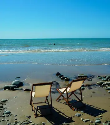 two chairs sitting in the sand on a beach at Lovely cottage in Snowdonia, private hot tub, by mountains & award winning beach in Fairbourne