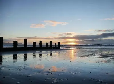 a pier on a beach with the sunset in the background at Harbourside 2 Bed apartment, Barmouth Bridge Views in Barmouth