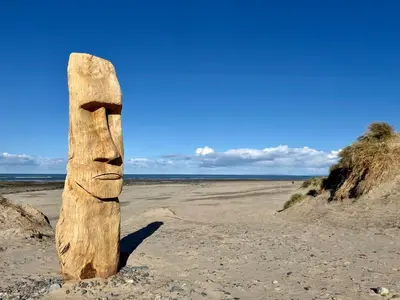 a totem pole in the sand on a beach at Deu-Ddrws in Barmouth