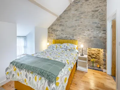 a bedroom with a large bed and a stone wall at Ivy Bush Cottage in Llanddewi-Brefi