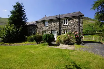 a stone house on a hill with a green yard at Pant in Llanymawddwy
