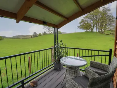 a porch with a table and chairs and a green field at Wild Acre in Llangadog