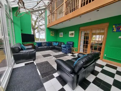 a living room with black leather furniture and green walls at Cringoed House in Aberaeron