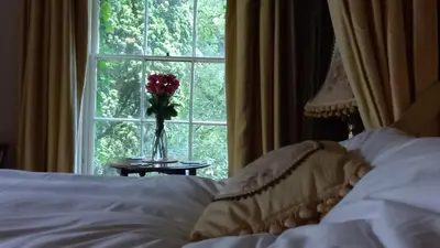 a bedroom with a bed and a window with a vase of flowers at Gelly Dylan Thomas Paradise in Lampeter