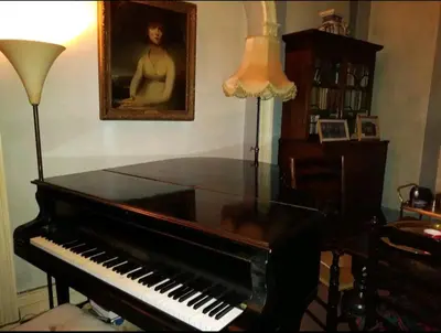 a piano in a living room with a lamp and a painting at Gelly Dylan Thomas Paradise in Lampeter