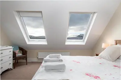 a bedroom with two windows and a bed with white sheets at The Barn in Bala