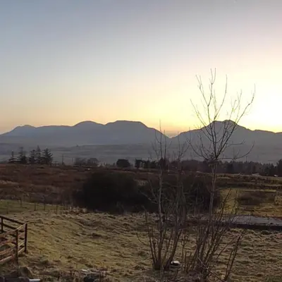 a sunset in a field with mountains in the background at Romantic Hideaway in Trawsfynydd