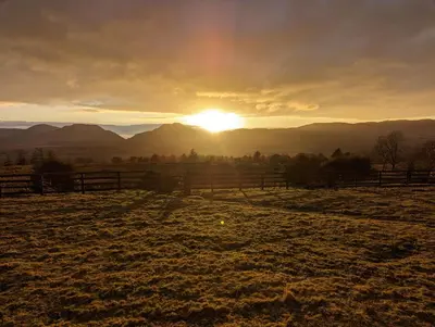 a field with a fence and the sunset in the background at Grade II Lodge House 2 Bedroom in Trawsfynydd